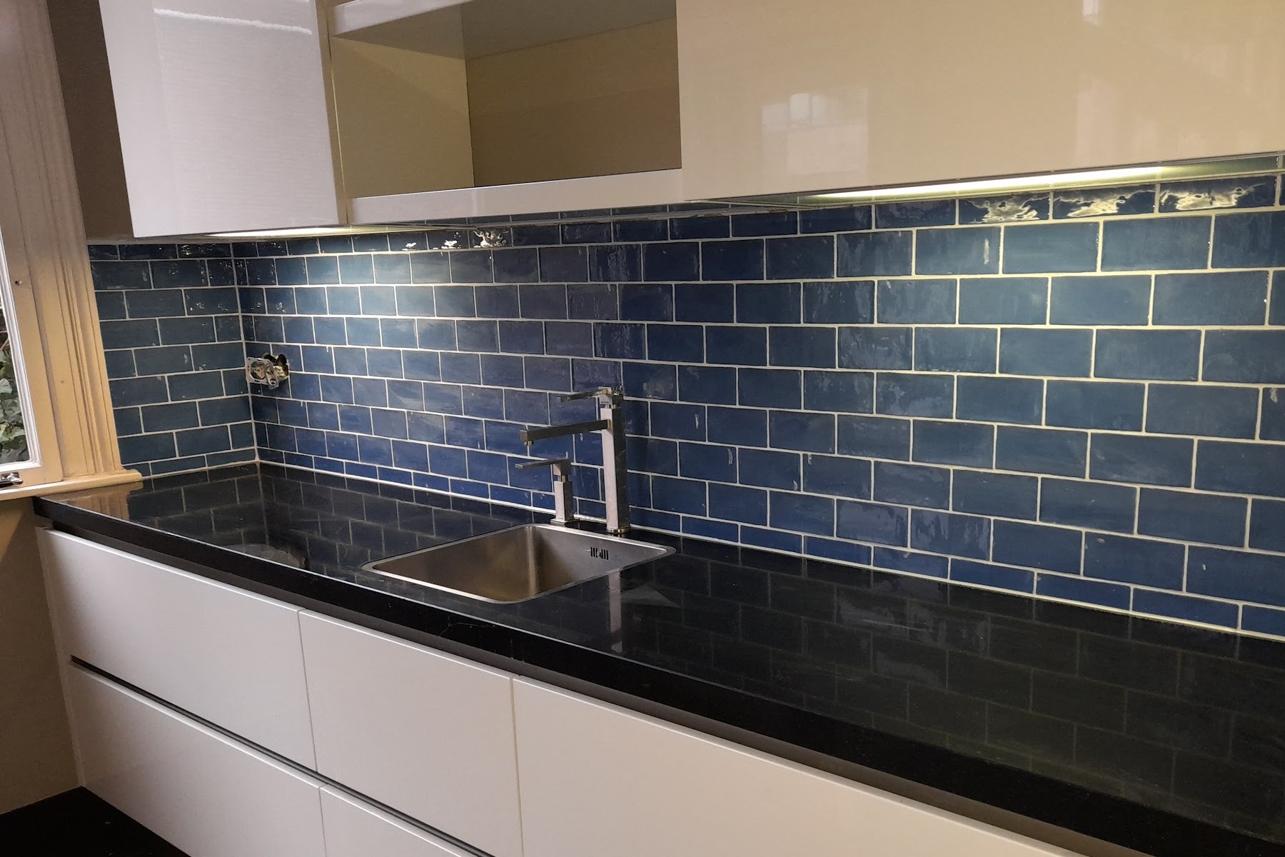 Keukenwand met blauwe metrotegels boven een zwart aanrechtblad, gezet door Tegelzetter B.K.